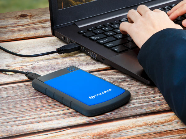 PRE-Loved - Transcend StoreJet 1TB Rugged Blue Portable Hard Drive - with Lightning-Fast Transfers next to a laptop.