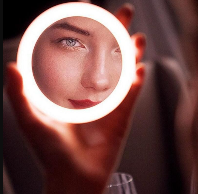 LED Portable Makeup Mirror with Built-in Wireless Charger - Rose Gold illuminating a woman's face for flawless makeup by Glamsmiths.