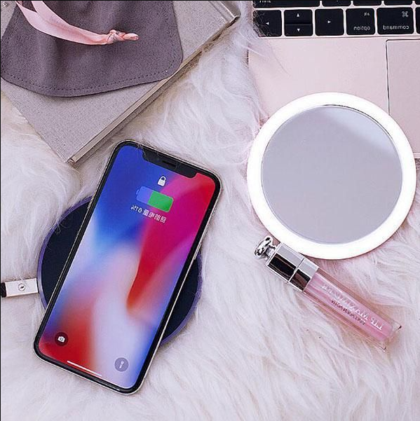Rose Gold LED Portable Makeup Mirror with Built-in Wireless Charger next to a charging phone and lip gloss on soft fur surface.