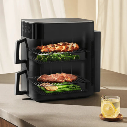 Black air fryer with food on a countertop next to a glass of lemon water.