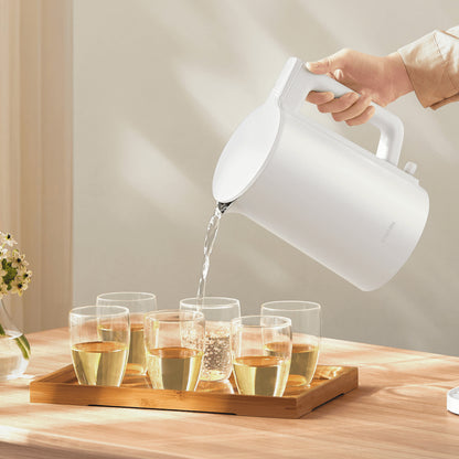 White electric kettle being used to pour water into glasses on a wooden tray.