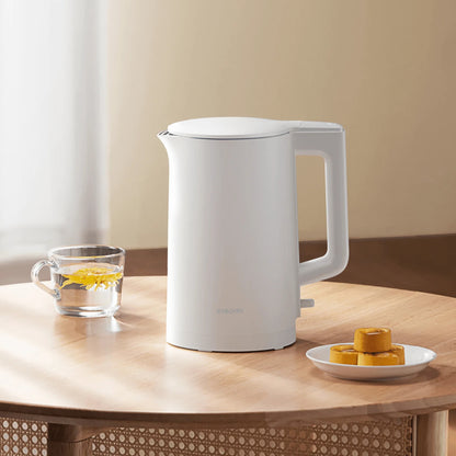 White electric kettle on a wooden table with a glass of lemon slices and a plate of cookies.