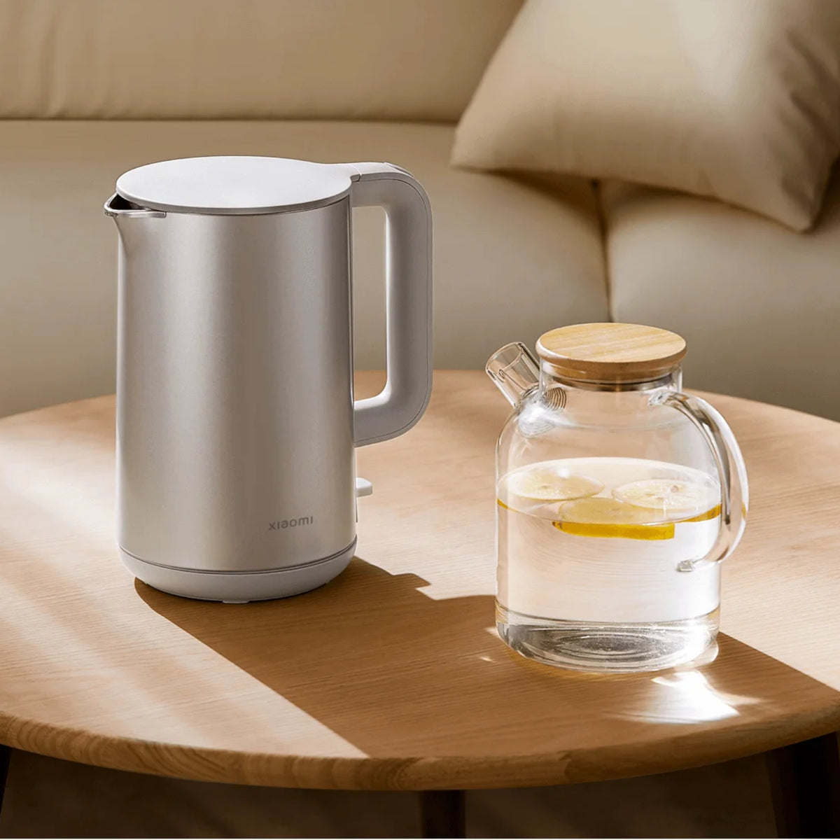Silver electric kettle and glass carafe with wooden lid on a wooden table.