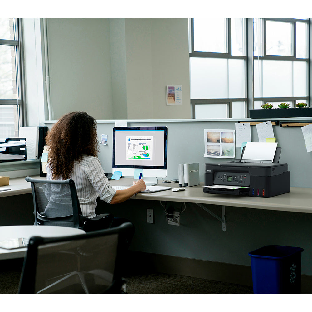 Person working at a desk with a computer and printer in an office setting