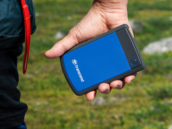 PRE-Loved - Transcend StoreJet 1TB Rugged Blue Portable Hard Drive - with Lightning-Fast Transfers in a hand outdoors.