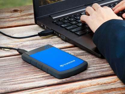 PRE-Loved - Transcend StoreJet 1TB Rugged Blue Portable Hard Drive - with Lightning-Fast Transfers next to a laptop.